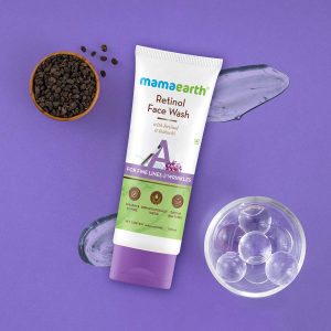 Mamaearth Retinol Face Wash tube (100 ml) placed on a purple background with visible gel texture swatches, a small bowl of translucent skincare capsules, and a bowl of dried Bakuchi seeds. The product label highlights ingredients like Retinol and Bakuchi, and mentions it is paraben & SLS-free, dermatologically tested, and suitable for all skin types.