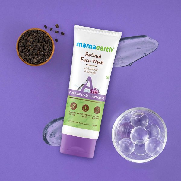 Mamaearth Retinol Face Wash tube (100 ml) placed on a purple background with visible gel texture swatches, a small bowl of translucent skincare capsules, and a bowl of dried Bakuchi seeds. The product label highlights ingredients like Retinol and Bakuchi, and mentions it is paraben & SLS-free, dermatologically tested, and suitable for all skin types.